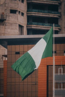 Nigerian flag fluttering against a modern city building backdrop, symbolizing national pride.