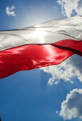A Polish flag flutters against a bright blue sky with clouds, symbolizing national pride.